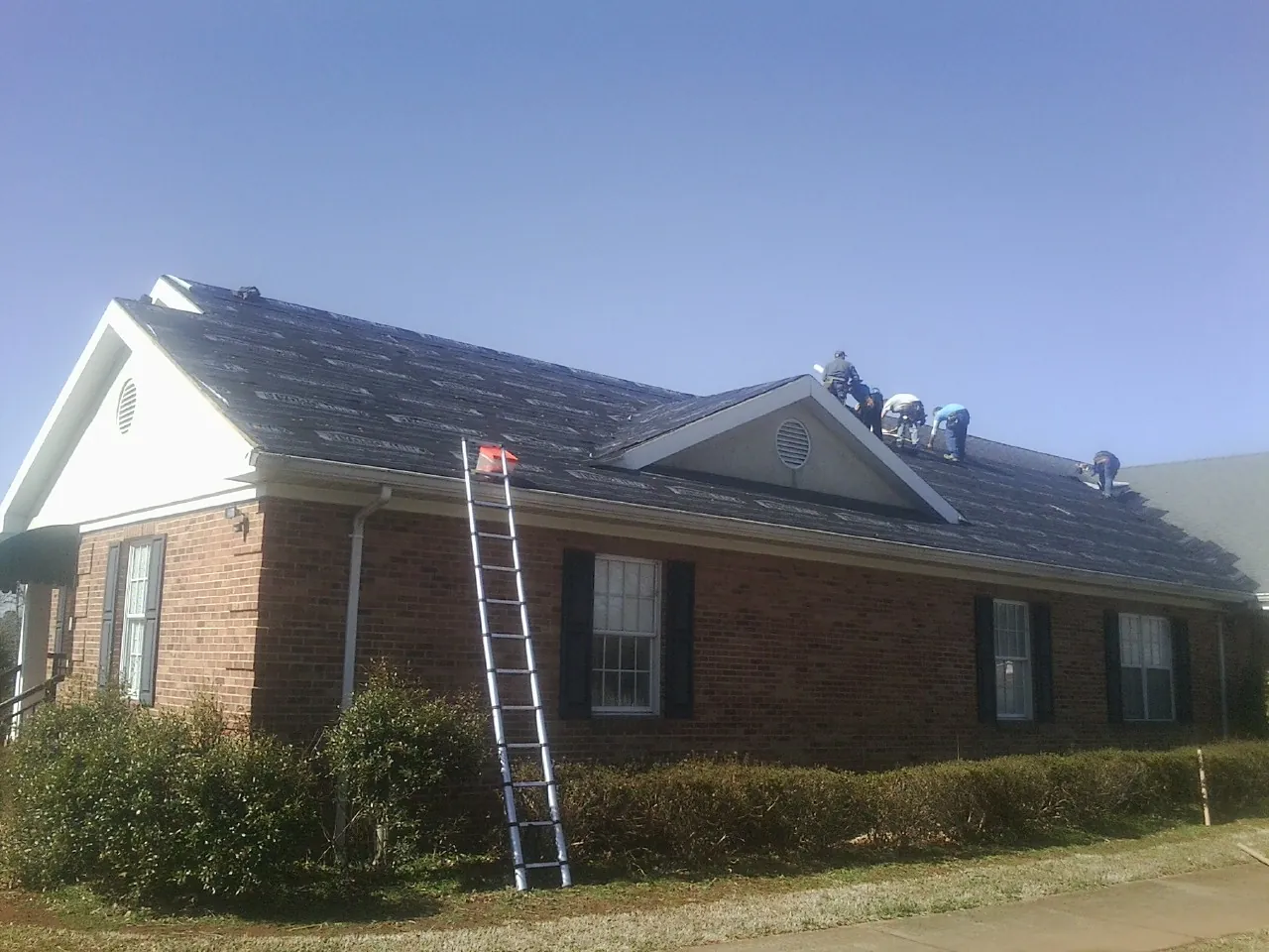 Crew tearing shingles off a brick ranch roof with a ladder set — Metal Roof Repair work by our crew in Stewart