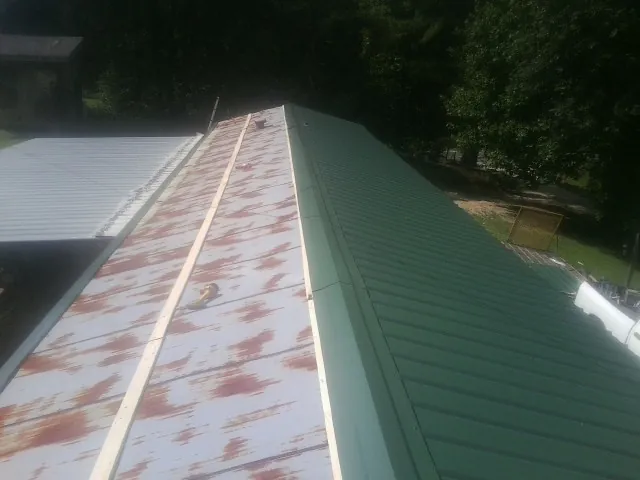 Old rusted panels beside newly installed green metal roofing — Wind Damage Roof Repair by Roofing Brothers in Stewart